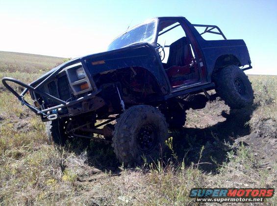 Dark blue Ford Bronco with off-road modifications, tilted on uneven terrain