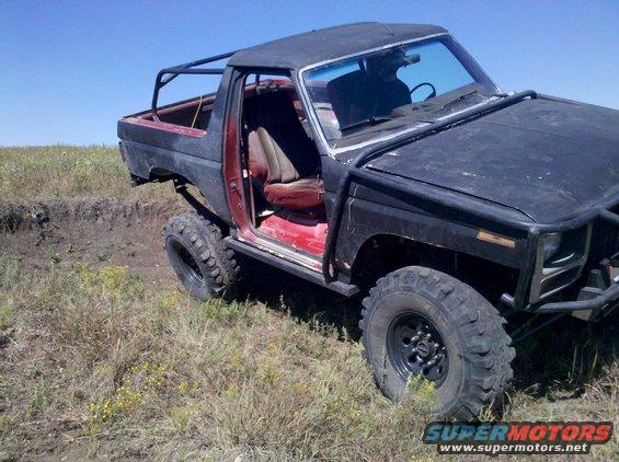 Modified off-road SUV with roll cage and open door, viewed from the front-three-quarter angle