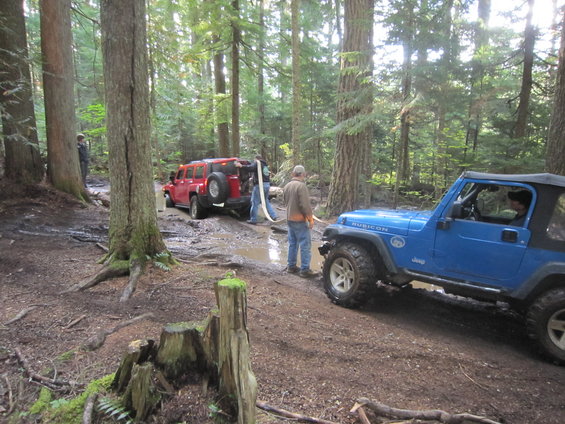 Blue Jeep Wrangler Rubicon parked on a muddy trail next to a red Hummer
