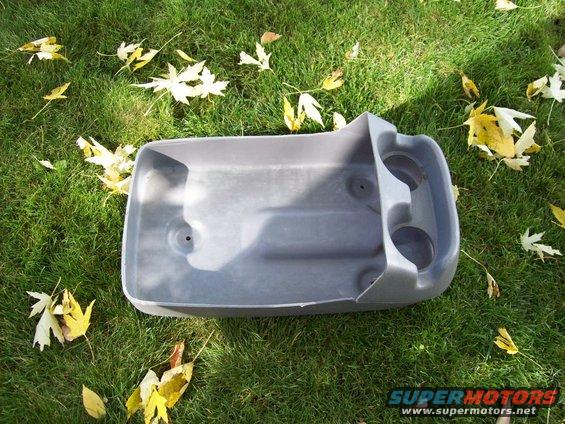 Gray plastic center console with two cup holders, lying on grass
