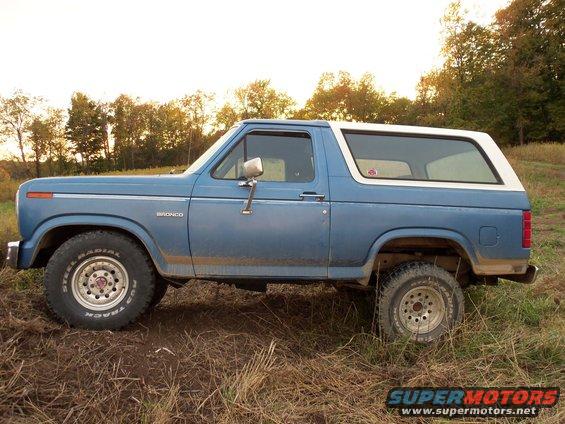 Side view of a blue and white 1985 Ford Bronco parked in a grassy field