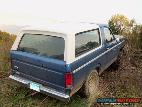 Blue and white Ford Bronco parked in tall grass, rear 3/4 view. License plate reads CUG 3375