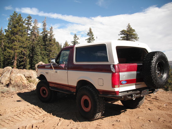 Two-tone maroon and white Ford Bronco with a spare tire mounted on the rear, parked on a dirt road