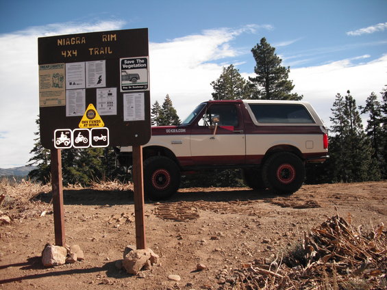 Red and white Ford Bronco parked by Niagra Rim 4x4 Trail sign