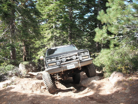 Black pickup truck with lifted suspension driving over rocks on a dirt trail