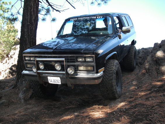 black SUV with off-road tires on rocky terrain, "UNDER CONSTRUCTION 4X4" sticker on windshield