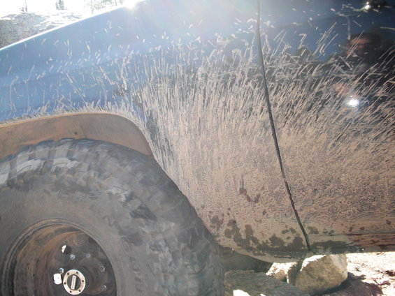 Mud splatters cover the side panel and fender of a dark-colored vehicle next to a large tire