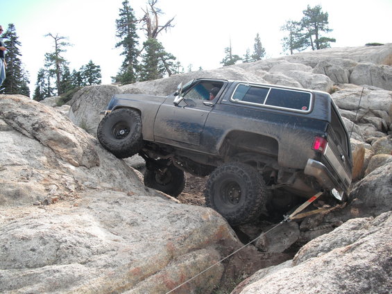 Dark blue off-road SUV with large tires climbing over large rocks on a trail