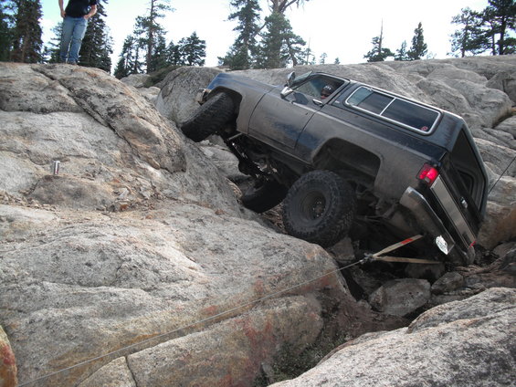 dark off-road SUV with large tires climbing over large rocks, one wheel lifted high