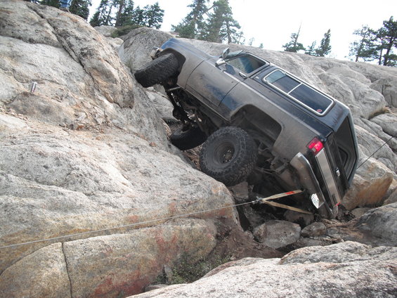 Dark blue off-road SUV tilted on a rocky incline with large tires and a winch strap attached