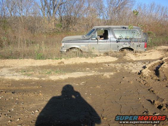 Gray 1991 Ford Bronco stuck in mud, side view. Driver visible inside