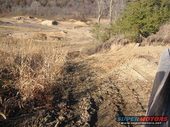 Dirt track leading into a quarry with dry grass and trees