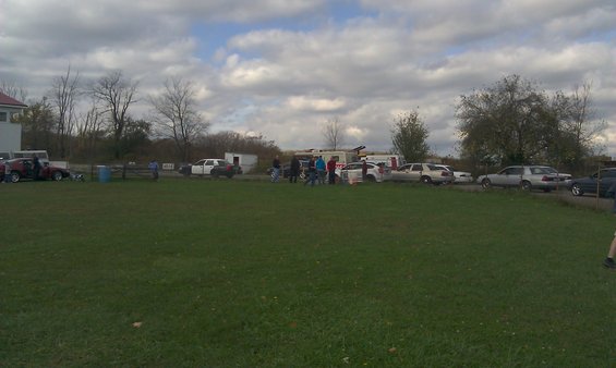 Several cars and a trailer parked on grass under a cloudy sky