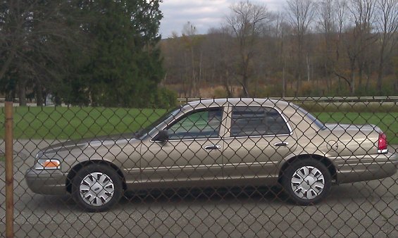 Tan 2007 Ford Crown Victoria parked behind a chain-link fence