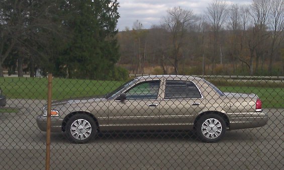 Gold 2007 Ford Crown Victoria parked behind a chain-link fence