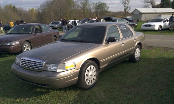 Gold Ford Crown Victoria with a number '3617' on the driver's side window, parked on grass
