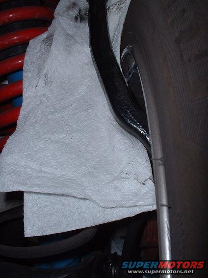 Suspension components with red coil spring, black control arm, and tire. Paper towel covers part of the suspension