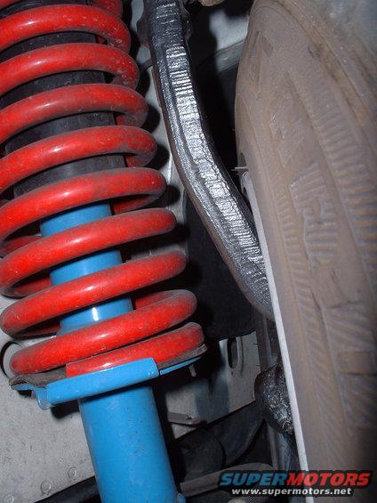 Suspension component with red coil spring and blue shock absorber, next to a tire