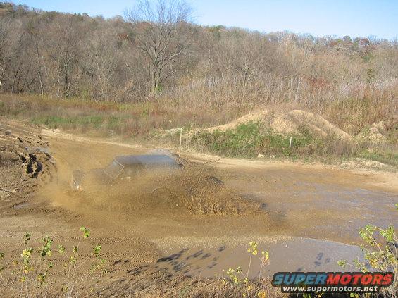 SUV driving through a muddy puddle, kicking up a lot of water