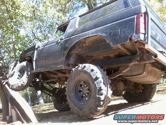 Modified Ford Bronco with large tires on a ramp, side view
