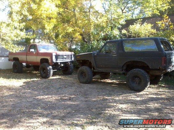 Lifted black Ford Bronco and lifted red and tan pickup truck parked outdoors