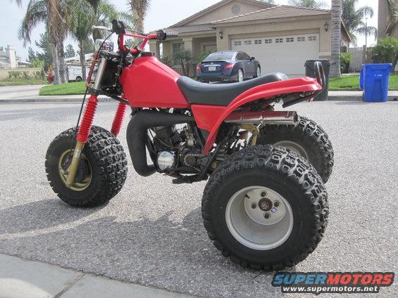Red three-wheeled ATV parked on a street in front of a house