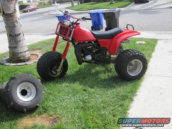 Red three-wheeled ATV parked on grass with a spare tire nearby