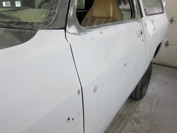 Side view of a white pickup truck body being prepped for paint. Shows door, fender, and interior seat