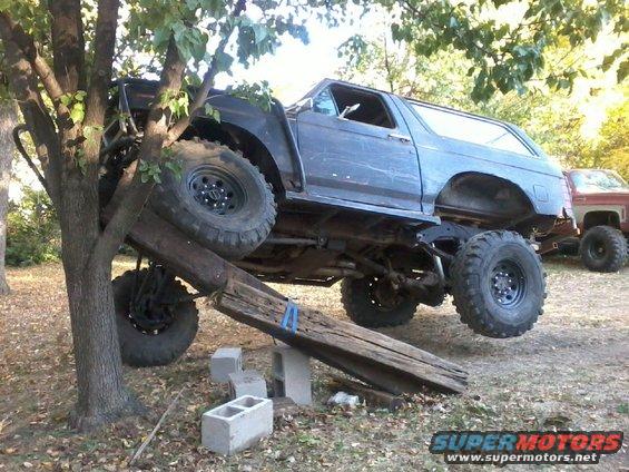 Ford Bronco on logs and cinder blocks, another truck in background