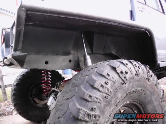 Close-up of a large off-road tire and suspension components, showing red coil springs and a shock absorber