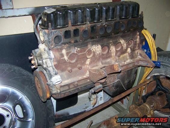 Jeep engine block with some accessories attached, sitting on a stand next to a tire