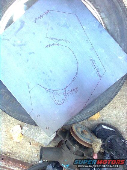 Sheet metal with a drawn template on top of a spare tire. Some engine parts and a shoe are nearby
