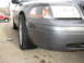 2004 Ford Crown Victoria - A gray Ford Crown Victoria with a flat tire is parked on concrete, with a red SUV in the background.