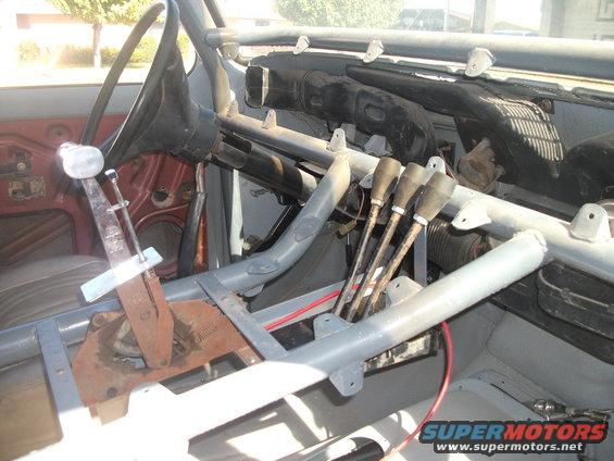 Interior of a vehicle with a roll cage, four shifters, and a steering wheel. The dashboard is visible