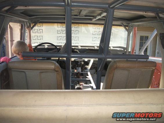 Interior view of a 1979 Ford Bronco with a roll cage and tan seats. A child is in the driver's seat