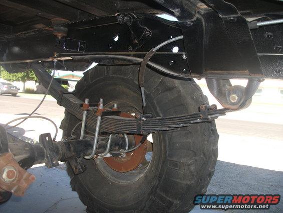 Underside of a vehicle showing the rear axle, large tire, and leaf spring suspension system