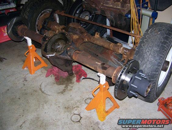 Rusted rear axle assembly with differential, brake rotors, and wheel hub, supported by orange jack stands