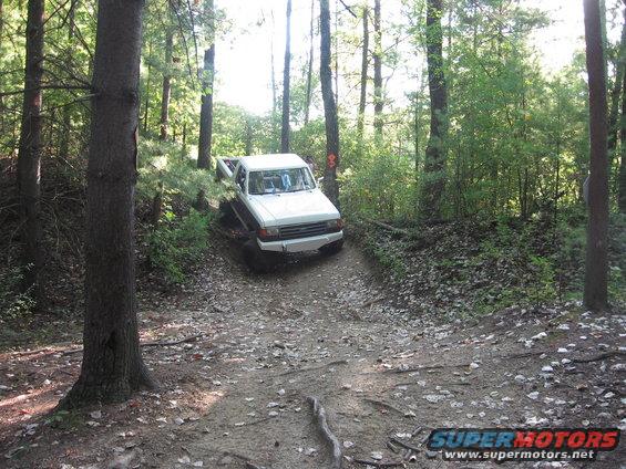 White pickup truck driving on a dirt path through a forest