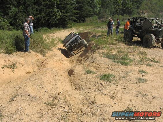 Off-road vehicle descending a steep dirt gully, with another vehicle and spectators nearby