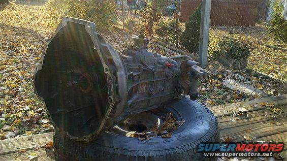 Transmission assembly resting on a tire outdoors, with fallen leaves scattered around