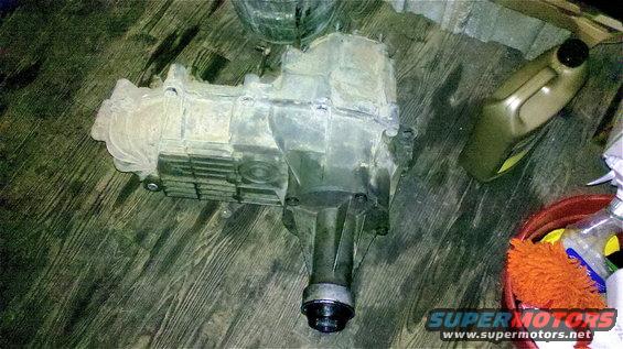 Dirty transfer case on wooden floor. Bottle of fluid and cleaning supplies nearby