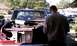 1979 Ford Bronco - A person stands in front of a red pickup truck with its hood open, revealing the engine compartment. Another vehicle is parked in the backg…
