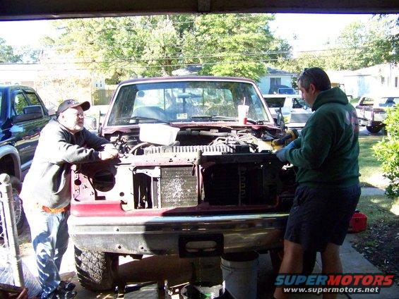 Red pickup truck front with hood open, engine exposed, two men working on it