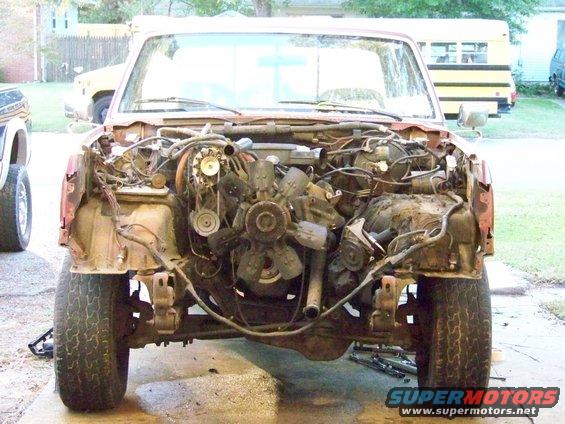 red pickup truck, front end removed showing engine and chassis components. Tires and suspension visible