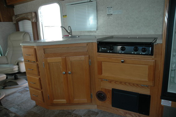 RV interior with wood cabinets, sink, stovetop, and a recliner