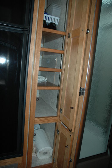 RV interior tall cabinet with shelves and doors, holding paper towels and a basket