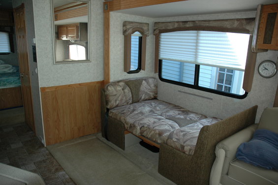 RV interior with a pull-out bed, wood paneling, and a mirror reflecting a cabinet