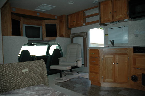 Interior of an RV showing the cab area with two seats, a swivel chair, and kitchen cabinets