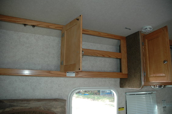 RV interior with open wooden cabinets and a window showing trees outside