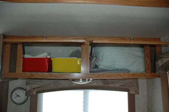 Overhead cabinets in an RV with red and yellow storage bins on the left and bedding on the right